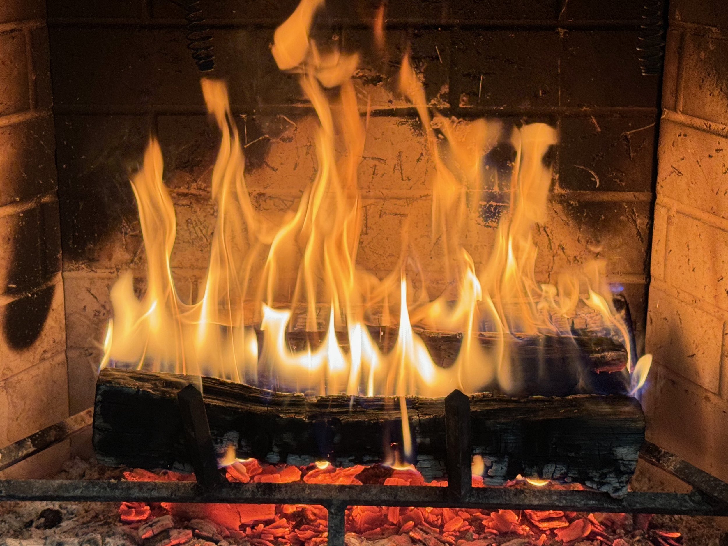 A nice roaring fire in a fireplace with a hot bed of coals underneath.