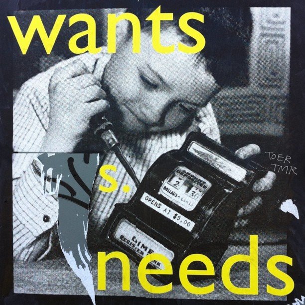 A street art poster of an old photo of a boy attacking a small cash register with a screwdriver with the words "wants" and "needs" superimposed on top of it in bright yellow letters