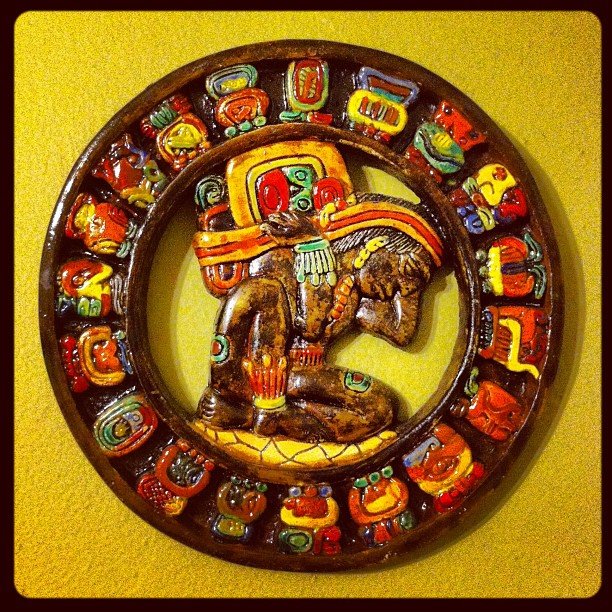 A ceramic round Mayan agricultural calendar painted in bold colors on a bright yellow wall