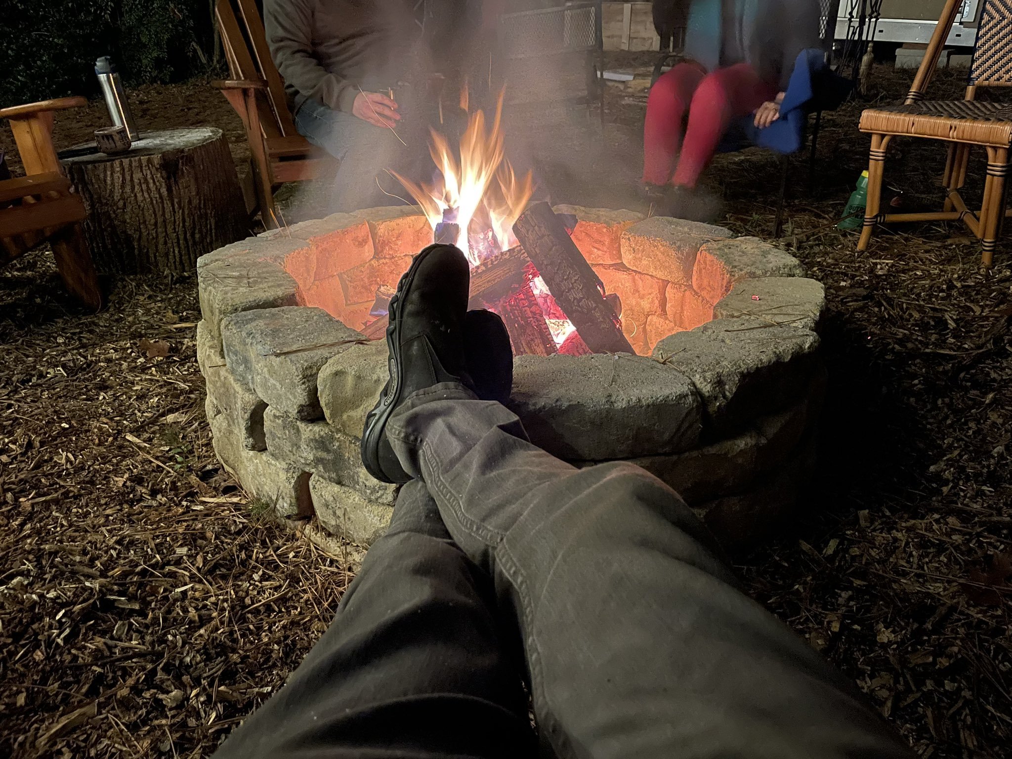 Legs and feet in front of a stone outdoor fire pit