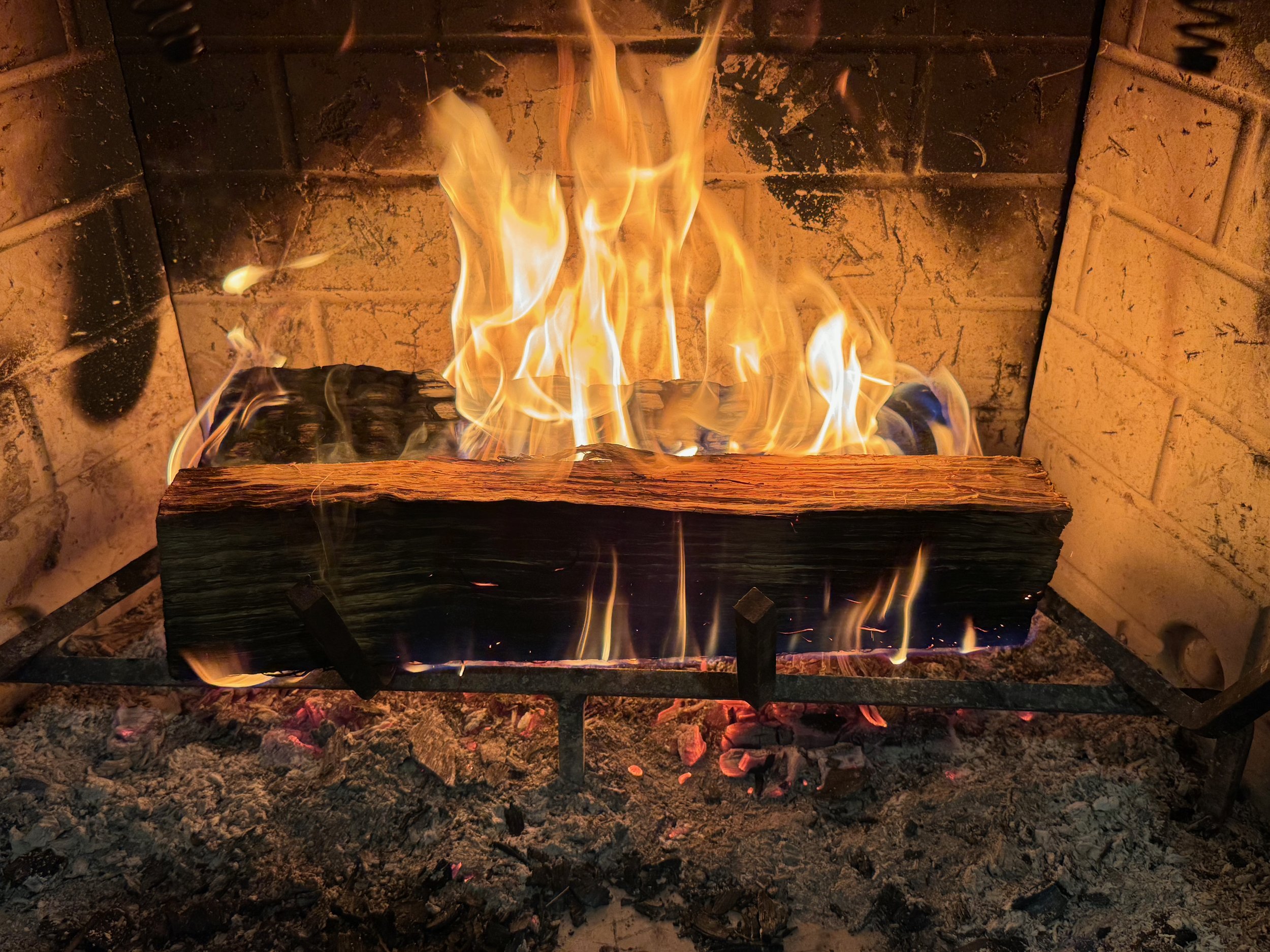 A fire in a fireplace with one well burned log in the back and one fresh one catching on fire in front.