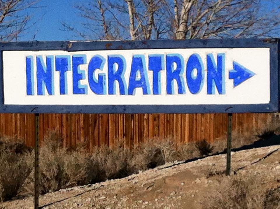 A sign in a scrubby desert landscape that reads "INTEGRATRON" with an arrow to the right