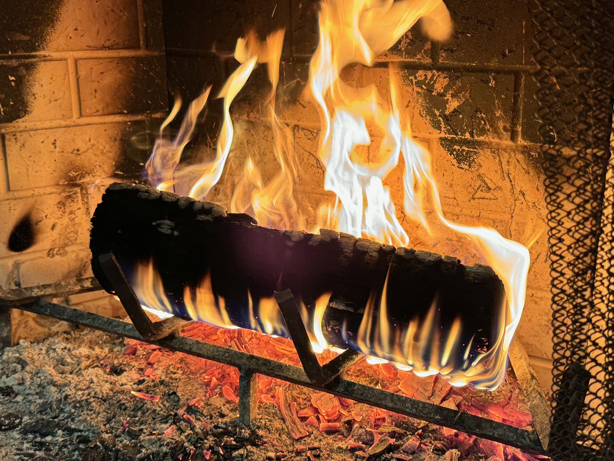 A nice, cozy, single-log fire in a fireplace with a bed of coals underneath.
