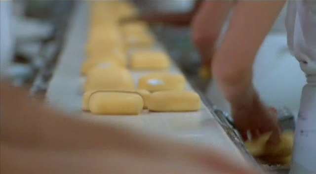 Twinkies rolling down an assembly line past the bare arms of factory workers