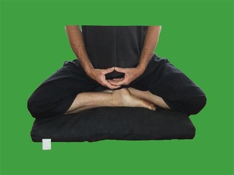 A photo of a person dressed in black sitting on a black meditation cushion with their legs in the Burmese posture and their hands in their lap in the Cosmic Mudra