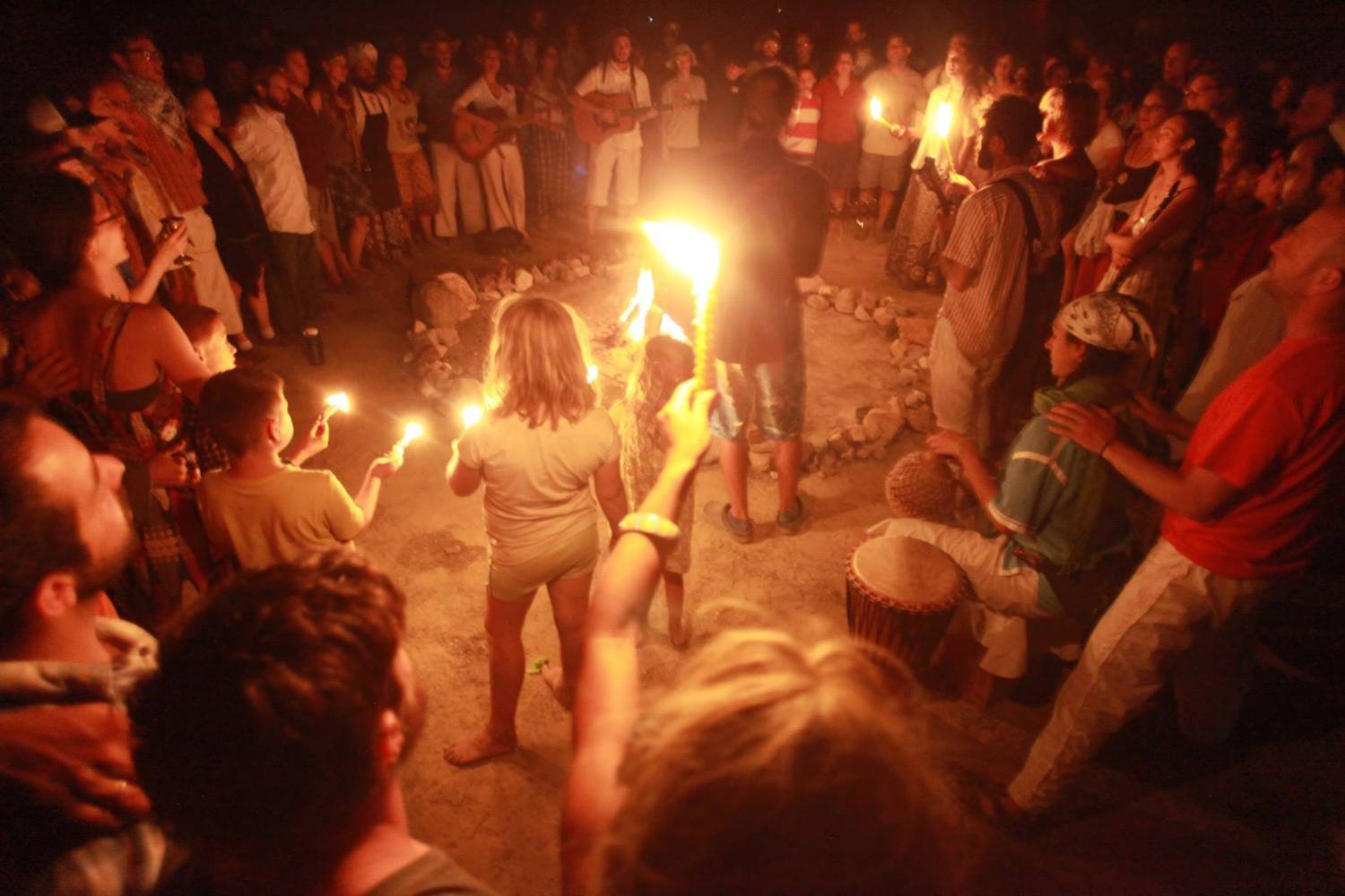 A circle of Jewish people observing Havdalah at night, holding candles and standing in a circle around a fire outside in the desert.