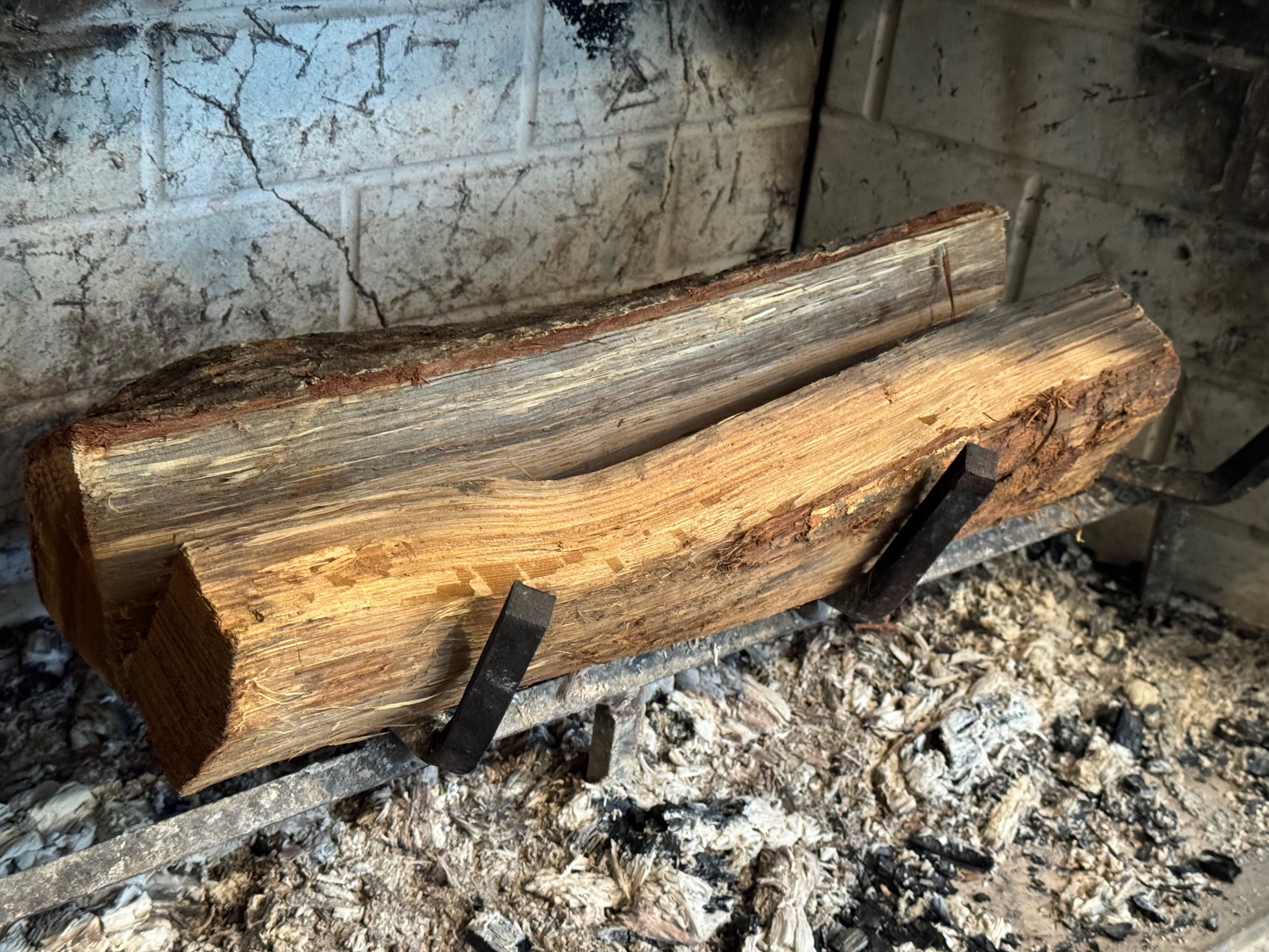 Two logs on a metal rack in a fireplace with flat edges touching at the bottom, forming a V-shaped channel down the length of the logs.