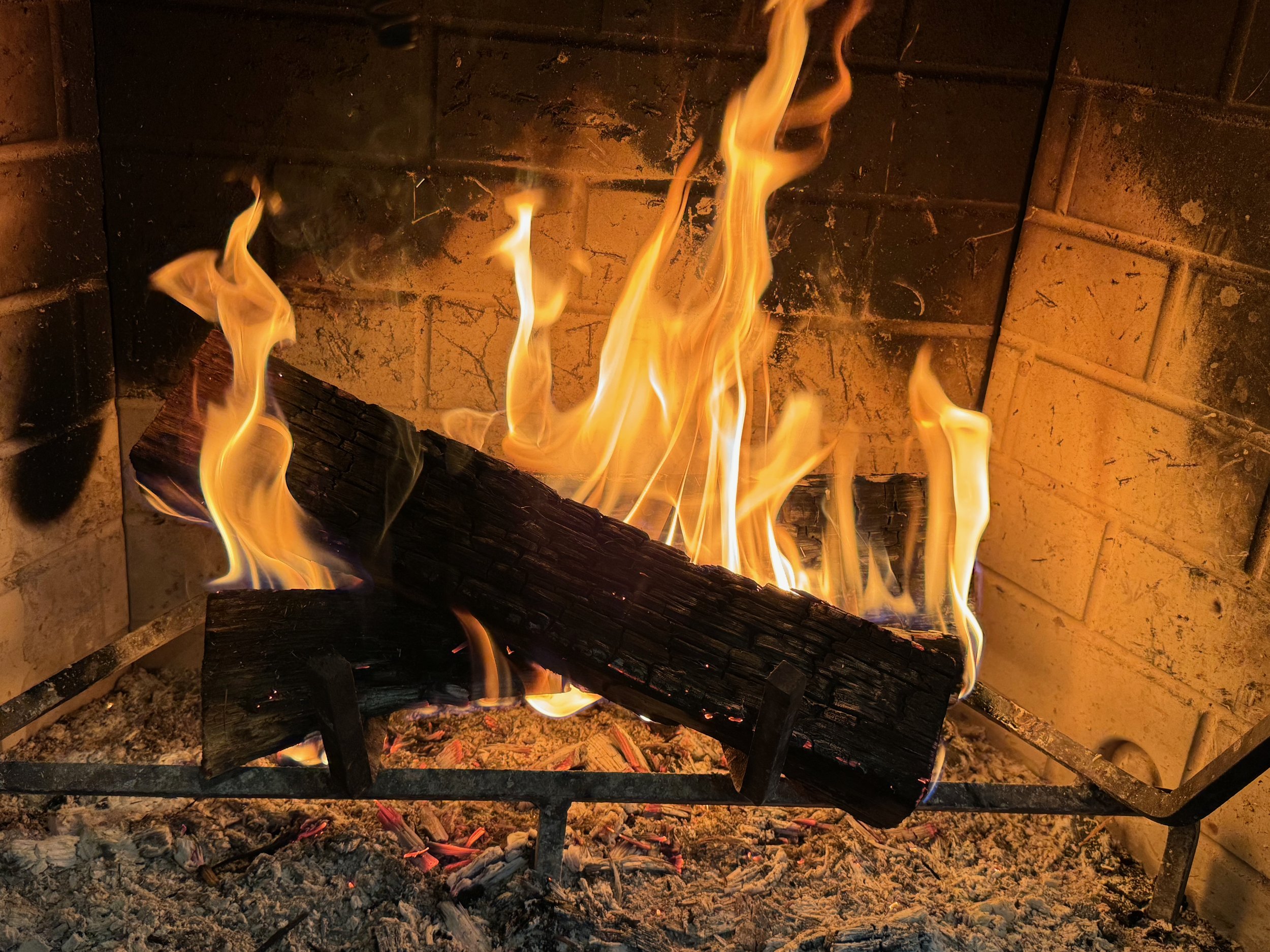 A fire in a fireplace with two logs burning flat and a third laid diagonally across the top