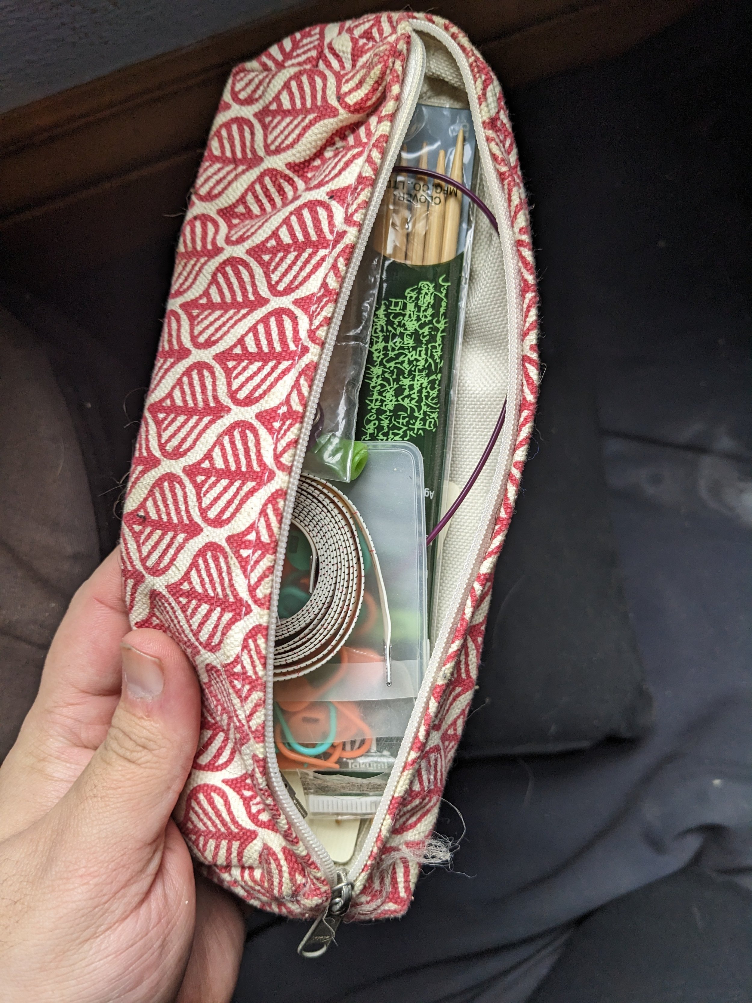 Photograph of a small white pouch with a red leaf pattern containing knitting supplies