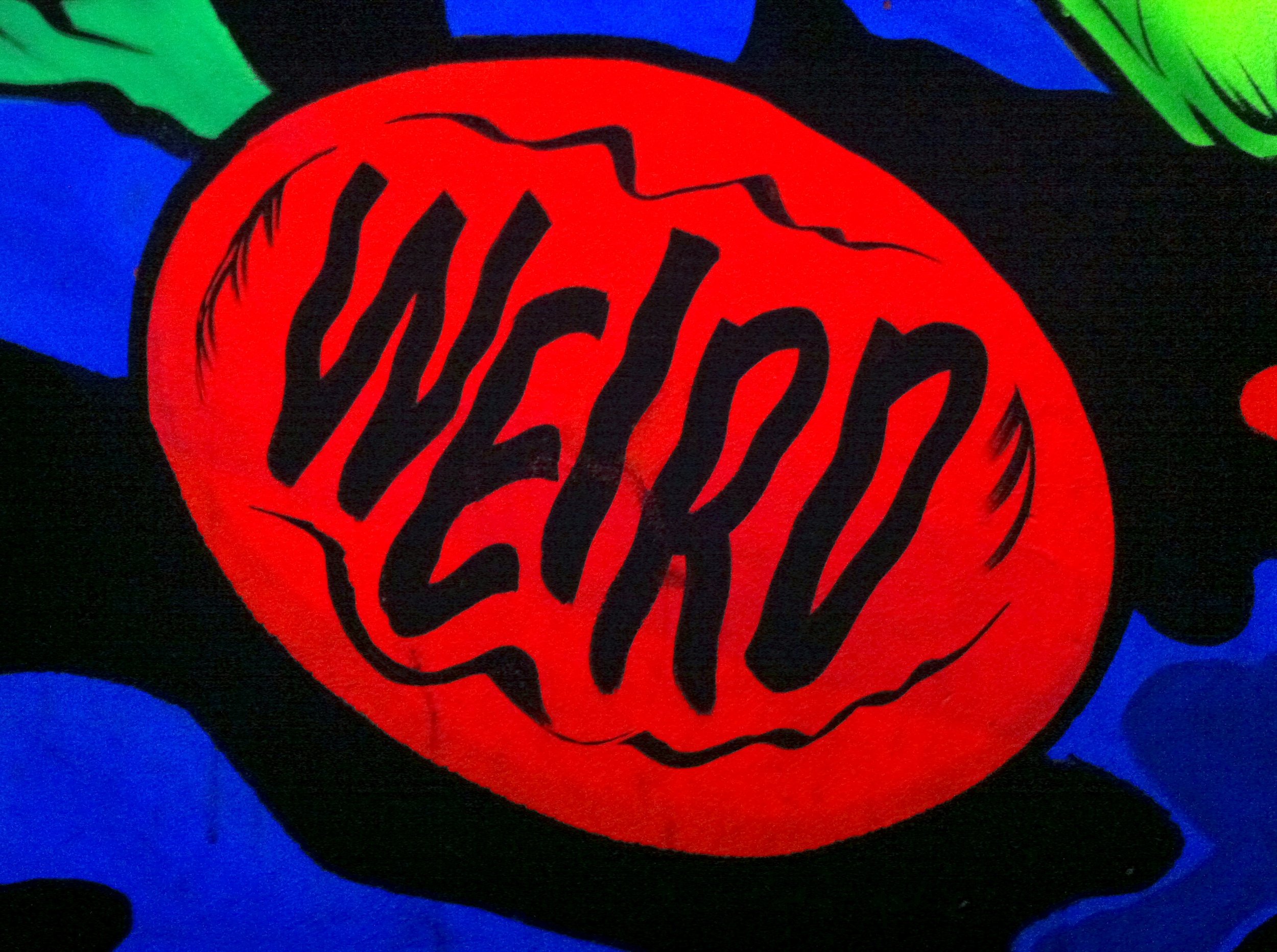 A red egg with the word "WEIRD" in black letters on it in front of a field of abstract black, blue, and neon green patterns